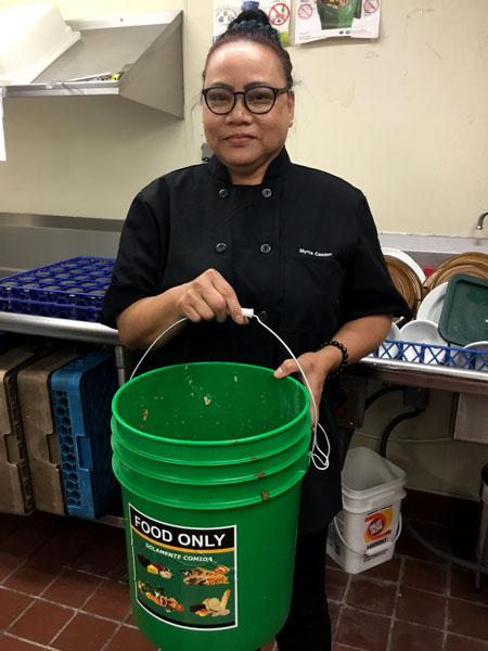 Myrna Casden holds a food waste bucket in the kitchen at Prestige Care Huntington Terrace.